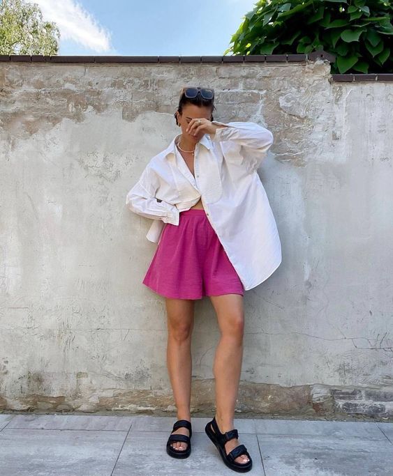 a minimalist summer look with an oversized white shirt, fuchsia shorts, black slides is cool for a hot day