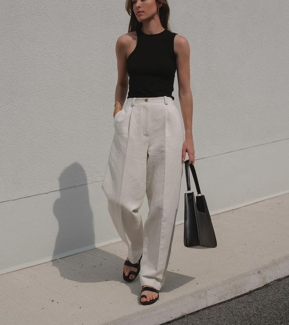 a minimalist black and white look with a black asymmetrical top, white wideleg pants, black sandals and a black bag