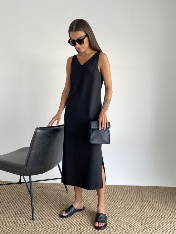 a minimalist total black look with a midi dress with a V-neckline, black slippers and a small clutch is work-appropriate