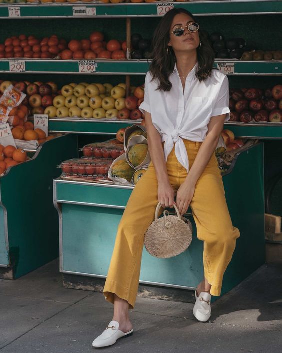 a white knotted short sleeve shirt, yellow cropped jeans, white slipper mules and a woven round bag for a summer vacation