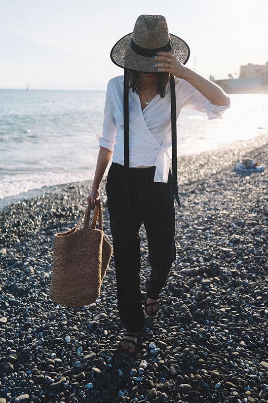 a white wrap blouse, black linen pants, black slide sandals, a black skinny scarf, a straw hat and a straw tote