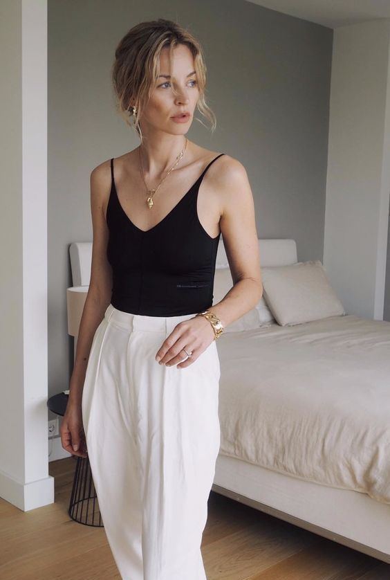 an elegant outfit with a black bodysuit, white high waisted pleated pants and a chic necklace is work-appropriate