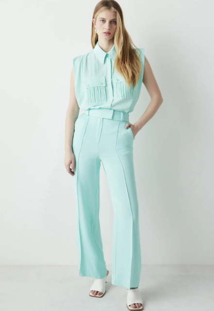 With silver earrings, mint green belted high-waisted flare pants and white leather heeled mules