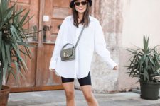 a casual look with an oversized white shirt, black biker shorts, black sneakers and a black bucket hat plus a grey bag