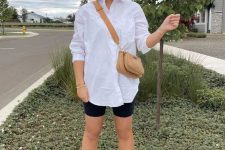 a casual summer outfit with an oversized white shirt, black biker shorts, white sneakers and a beige mini bag