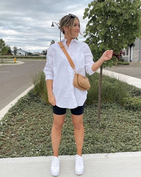 a casual summer outfit with an oversized white shirt, black biker shorts, white sneakers and a beige mini bag