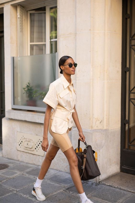 a catchy neutral look with a safari style neutral shirt, beige biker shorts, white snakers and socks, a brown bag
