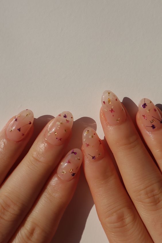 a delicate blush manicure with small dried flowers and gold leaf touches is perfect for both spring and summer