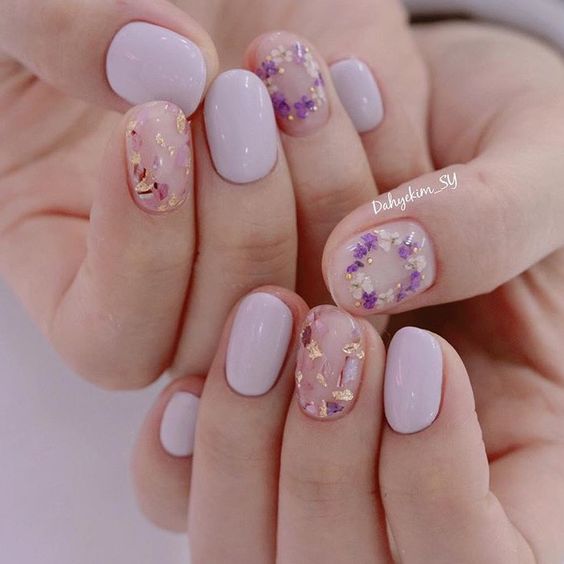 a lovely spring manicure with pale pink and blush nails, blush ones are accented with purple and blush dried blooms and gold touches