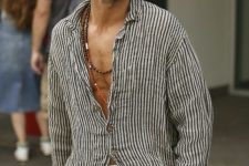 a relaxed vacation look with a striped linen shirt, grey pants, layered beaded necklaces and sunglasses