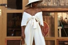 a stylish vacation look with a white off the shoulder knotted crop top and matching pants, black slippers and a hat