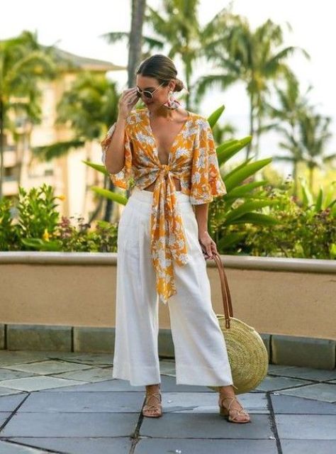 a vacation outfit with a bold yellow printed wrap crop top with bell sleeves, white linen pants, metallic shoes and a woven bag