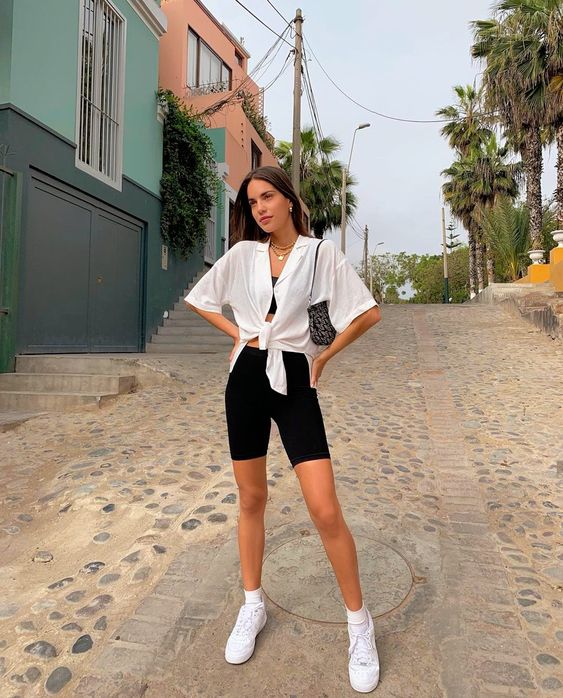 an effortless and comfy look with a black crop top, biker shorts, a white knotted shirt, white sneakers and white socks