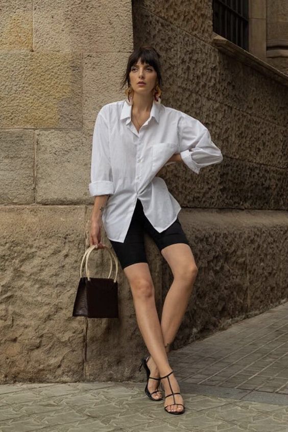 an elegant summer outfit with black biker shorts, an oversized white shirt, black strappy heels and a black bag with statement handles