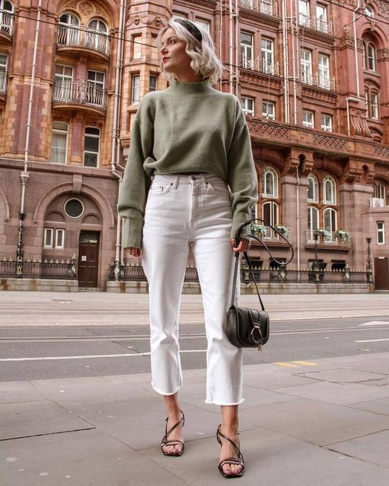 a chic fall outfit with a green turtleneck sweater, white cropped jeans, strappy black shoes and a small green bag