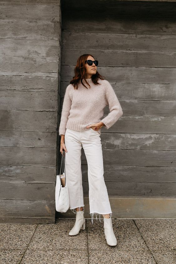 a neutral fall outfit with a neutral sweater, flare cropped jeans, white booties and a white bag