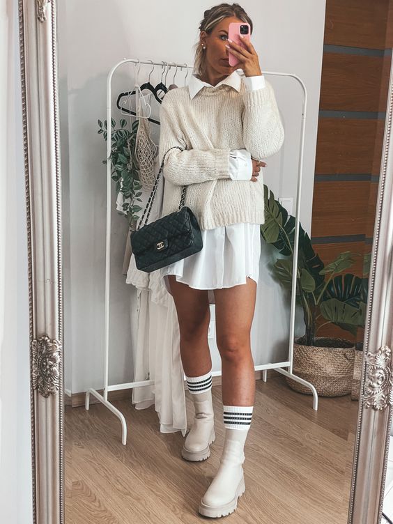 a white mini shirtdress, a white jumper over it, white chunky Chelsea boots, white socks and a small black bag