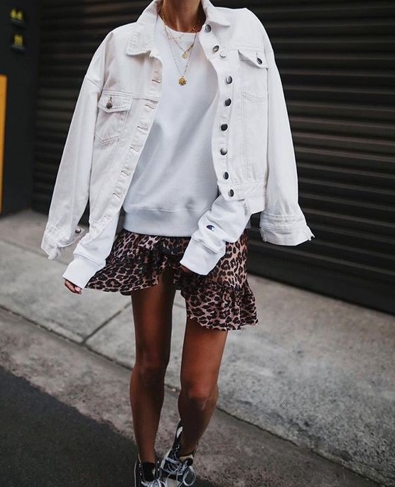 a white sweatshirt, a leopard mini skirt, a denim jacket, black trainers and layered necklaces