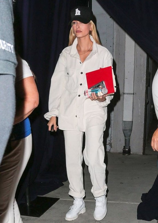 white jeans, a white denim jacket, white trainers and a black cap worn by Hailey Baldwin