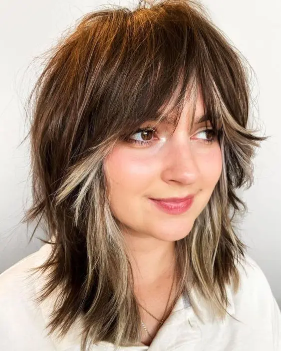 a choppy haircut with a dark brunette tone and blonde peekaboo hair to frame the face and make it stand out a lot