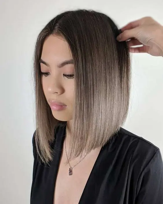 a cool mousy brown angled bob haircut with central parting and an ombre effect from darker root to mousy brown on the ends