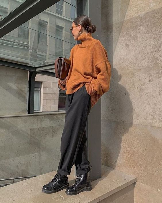 a minimalist look with a touch of bright color, an orange oversized sweater, black pants, black boots and a brown bag