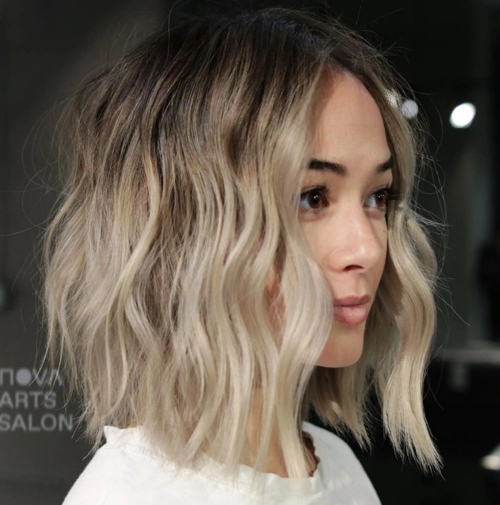 a wavy and textured blonde long bob with an A-line and a darker root looks super cute, chic and lovely