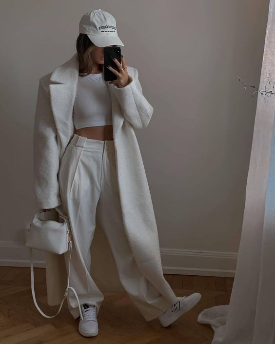 a white crop top, white high waisted trousers, sneakers, a creamy maxi coat, a cap and a small bag for the fall