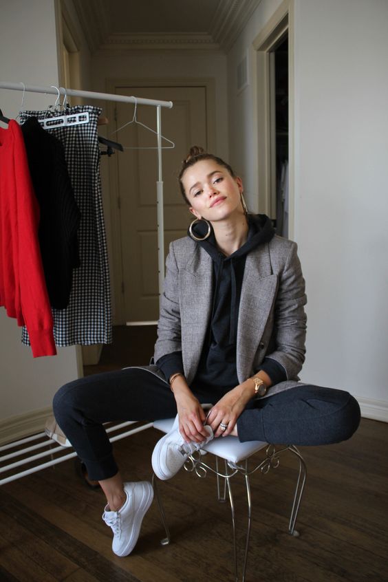 a relaxed work outfit with a black hoodie and sweatpants, a grey blazer, white sneakers and statement earrings