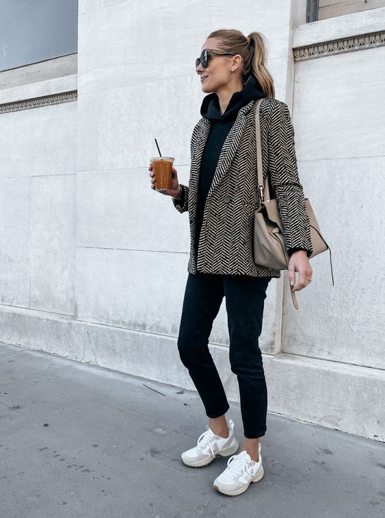 a stylish and relaxed work look with a black hoodie, black cropped jeans, a printed blazer, white trainers and a beige bag