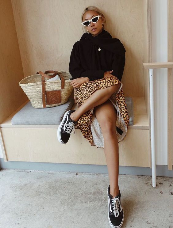 a black hoodie, a leopard print midi skirt, black sneakers and a woven bag are a cool combo for a cold day