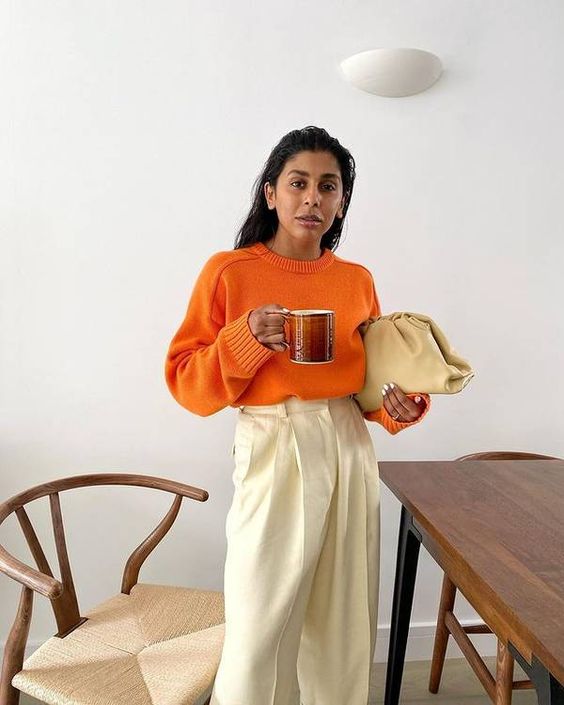 a pretty and bold fall outfit with an orange jumper, neutral trousers, a neutral clutch bag is amazing