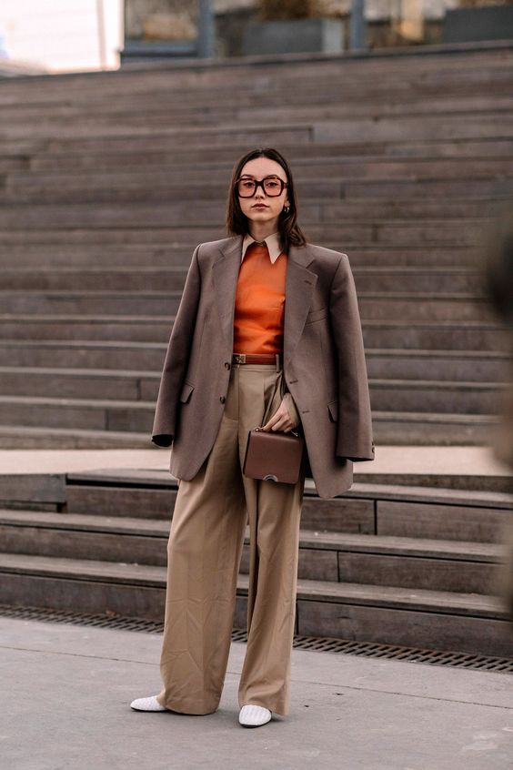 a stylish fall work outfit with a white shirt, an orange jumper, beige pants, a brown blazer, a brown bag and white shoes