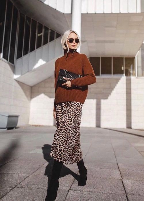 a rust-colored turtleneck sweater, a leopard printed midi skirt, black boots and a large black clutch for the fall to winter look