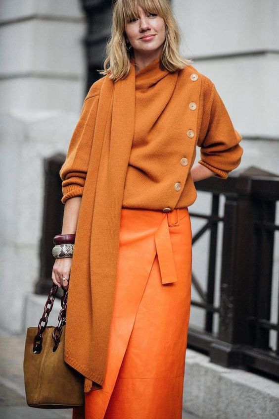 a sophisticated fall outfit with an orange jumper and a scarf, a bold orange wrap midi skirt, brown shoes and a mustard bucket bag
