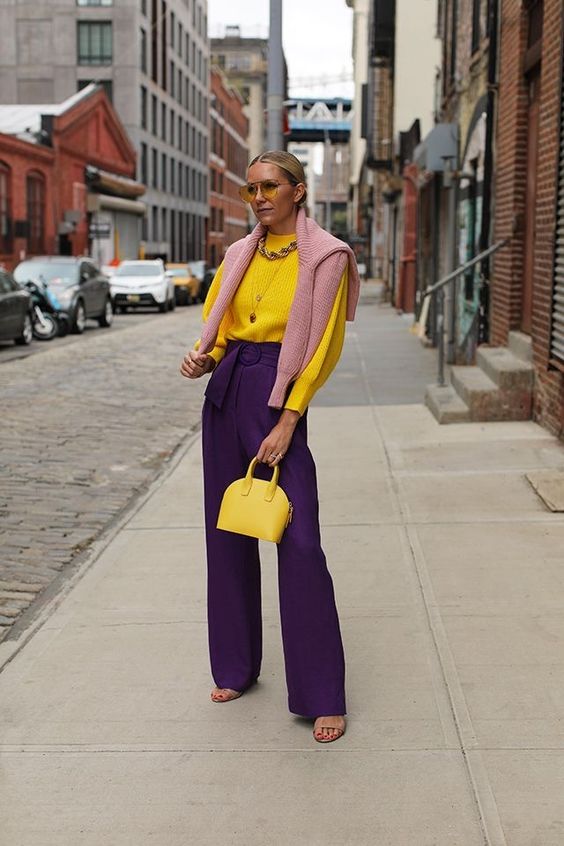 a bright fall work look with a yellow ribbed jumper, deep purple pants, a pink jumper over the shoulders, a yellow bag and nude shoes