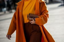 26 a fall tone work outfit with a yellow turtleneck, brown trousers, an orange coat, a brown bag and white shoes