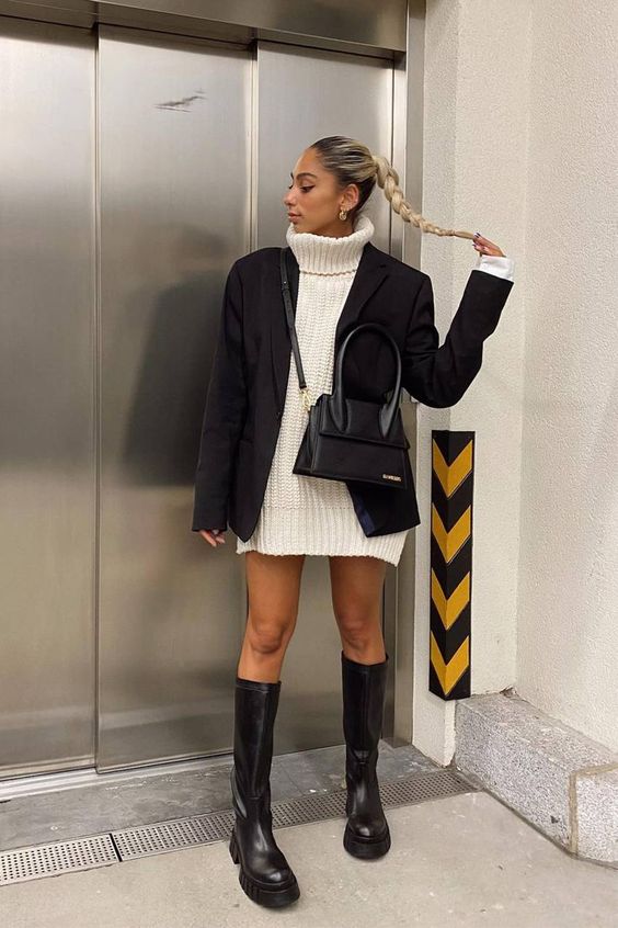 a white chunky knit sweater dress, an oversized black blazer, black chunky knee boots, a black bag create a contrasting fall look