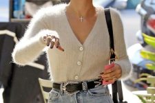 Hailey Bieber wearing a neutral cardigan tucked into light blue jeans, a black belt and a black woven bag