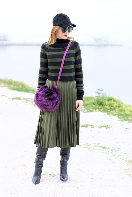 With navy blue and green striped turtleneck sweater, black baseball cap, green pleated midi skirt, sunglasses and black leather high boots