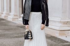 With sunglasses, golden earrings, white high-waisted pleated midi skirt, black and white mini bag and black patent leather ankle boots