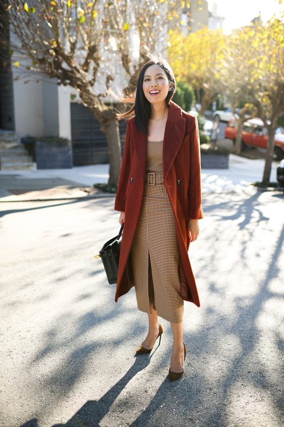 a beige cami rop, a plaid midi pencil skirt with a front slit, brown velvet shoes, a rust-colroed coat and a black bag
