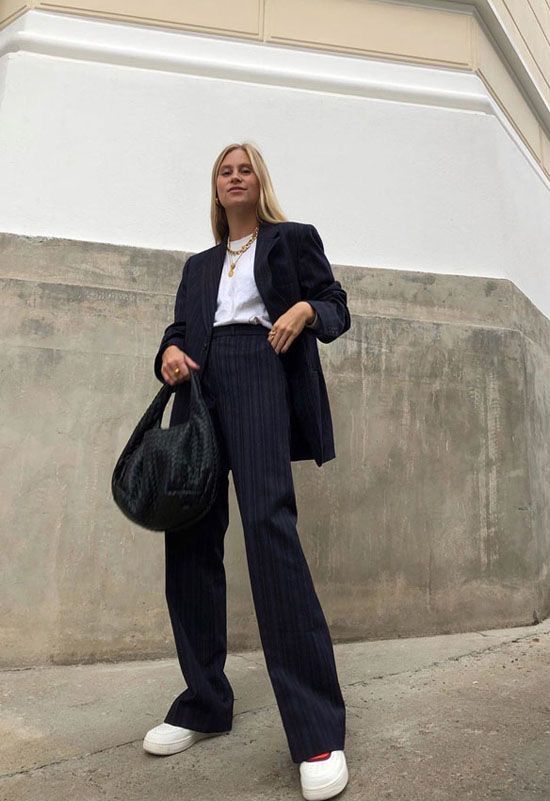 a chic black thin stripe pantsuit, a white t shirt, layered necklaces, white platform sneakers and a black bag