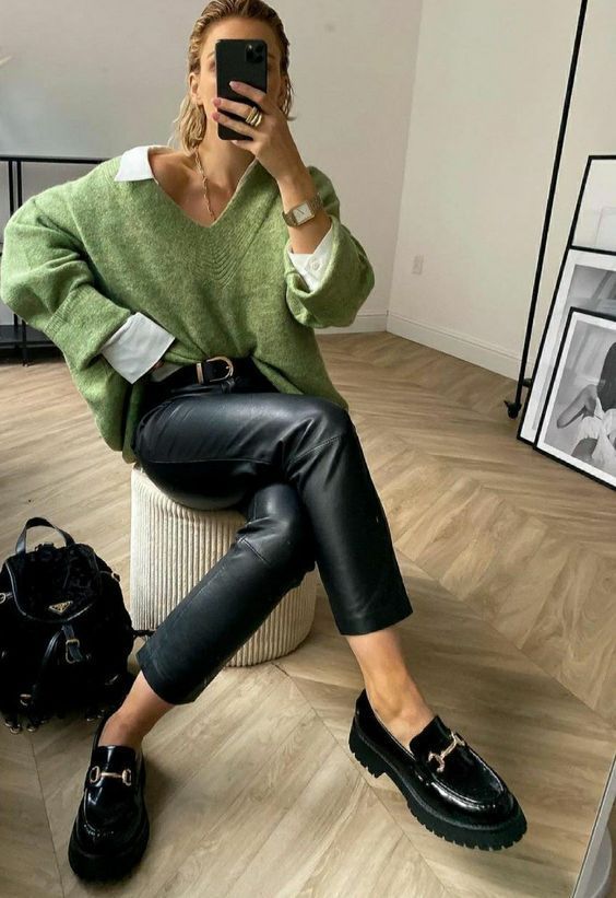 a chic fall look with a white oversized shirt, a green V-neck sweater, black leather pants, black loafers and a black backpack