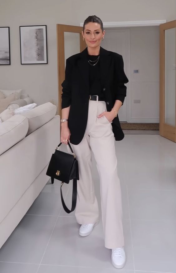 a classy monochromatic work outfit with a black t-shirt, creamy high waisted pants, white sneakers, an oversized black blazer and a black bag