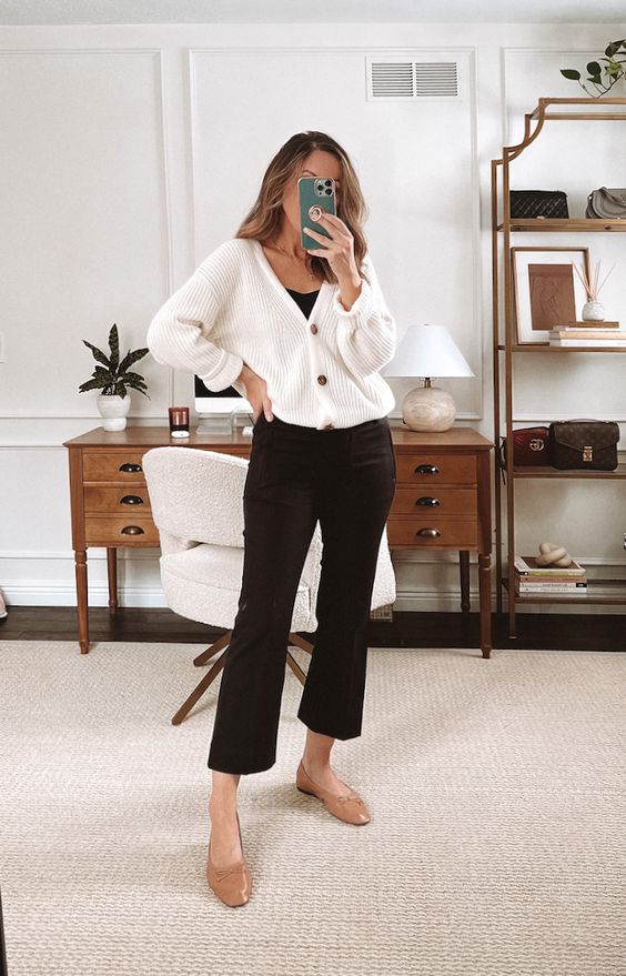a contrasting fall work look with a black top and black flare pants, a white cardigan, beige flats