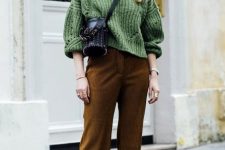 a fall outfit with a green chunky knit sweater, brown pants, a black bucket bag is chic and cozy