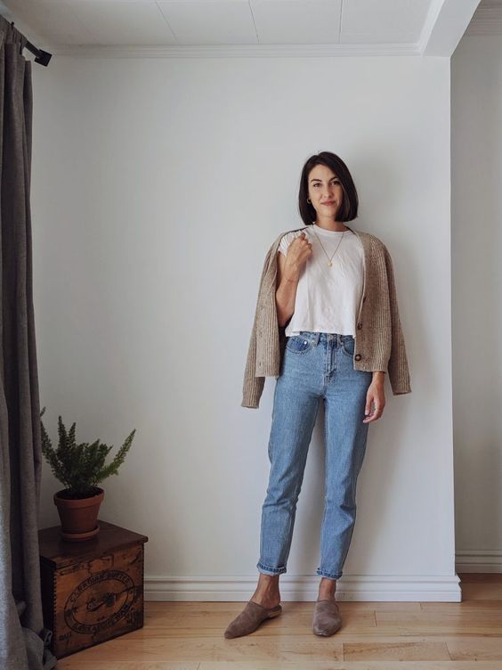 a neutral fall outfit with a white t-shirt, blue cropped jeans, a neutral cardigan, grey slippers