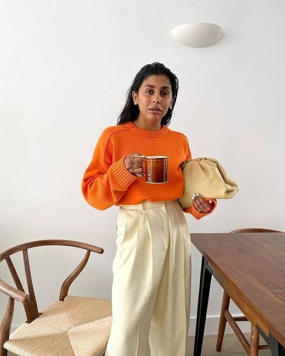 a pretty and bold fall outfit with an orange jumper, neutral trousers, a neutral clutch bag is amazing