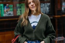 a printed t-shirt, a dark green cardigan tucked into blue jeans, a red bucket bag for a relaxed fall work look